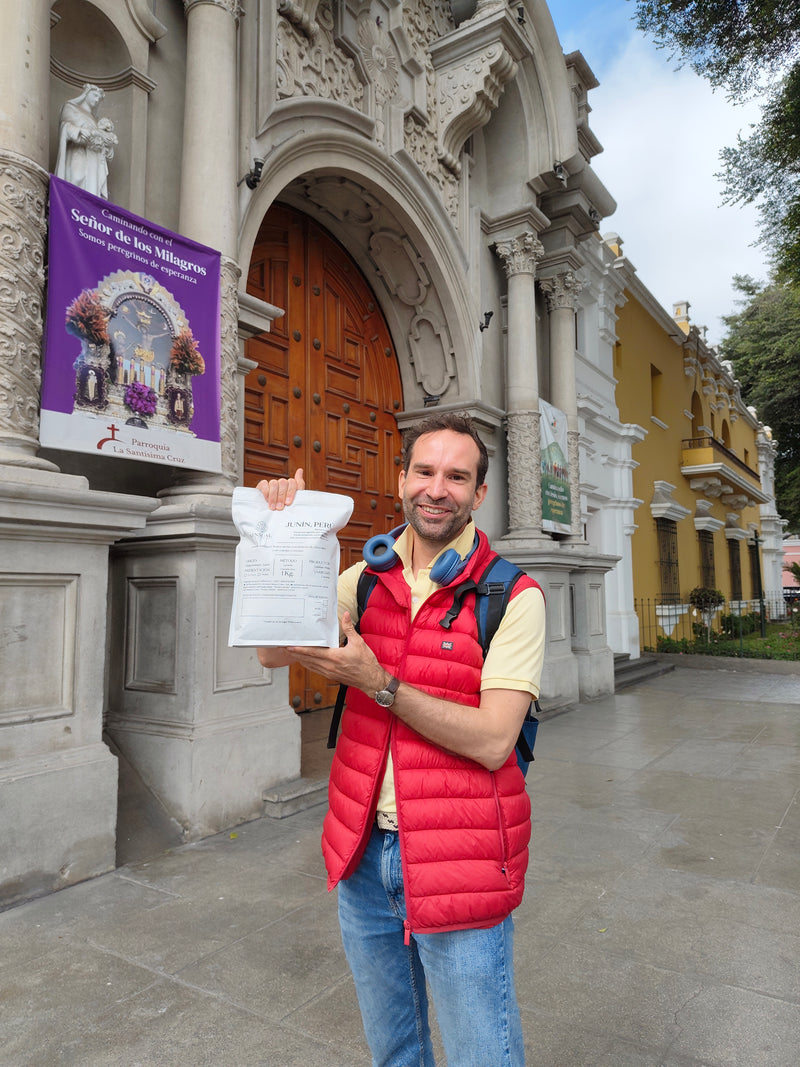 Man standing with Sensual Coffee bag in front of a church in Barranco, Lima, Peru.
