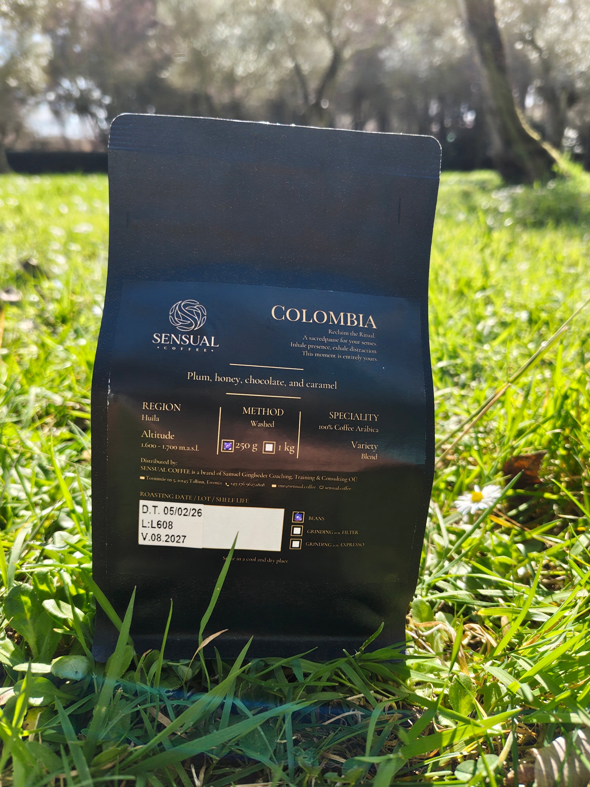 Coffee bag labeled 'Colombia' by 'Sensual' on grass with trees in the background