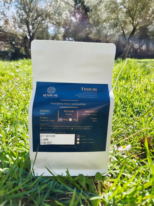 Coffee bag labeled 'Timor' on grass with trees in the background