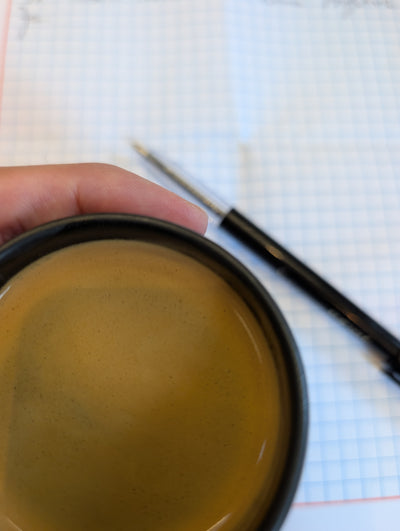 A creamy cup of Espresso with a pen and paper in the background - coffee as a ritual